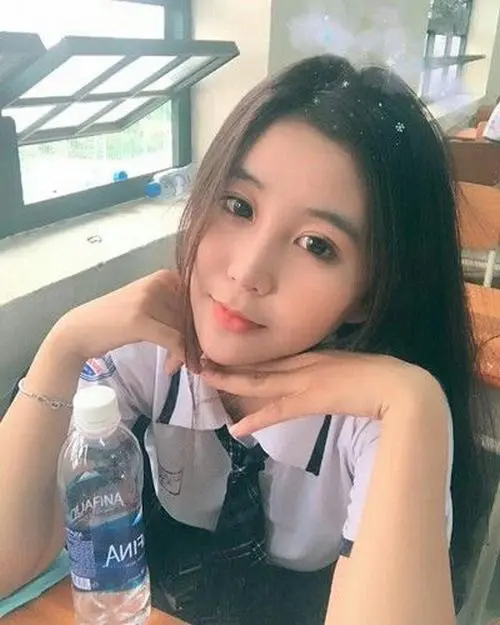 39 Ảnh avatar nữ sinh cô gái tóc dài ngồi bên bàn với chai nước trong tay, chống cằm nhẹ và cười bằng mắt, ánh sáng trong quán làm ảnh k5 trông đẹp mà không bị gắt