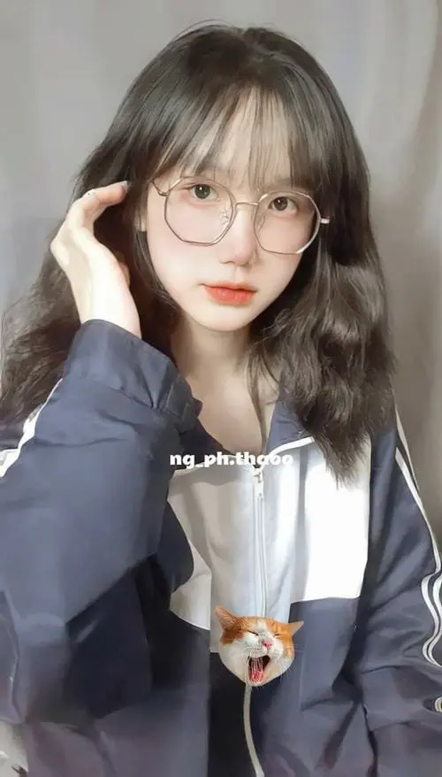 42 Bạn nữ tóc nâu đeo kính mặc áo sáng màu ngồi trong quán, tay ôm chú gấu nhỏ và cười dịu, kiểu chụp k5 này vừa gần gũi vừa hợp với ảnh đại diện mềm mại