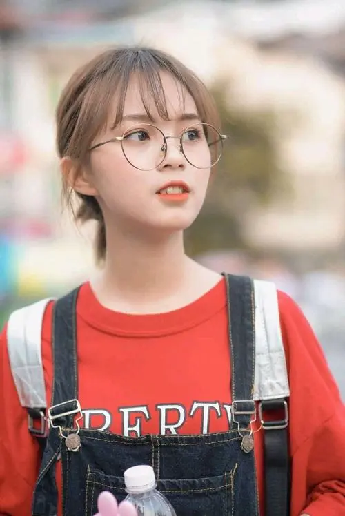 35 Hình profile đời thường cô gái đeo kính mặc áo đỏ đeo balo, chụp nửa người giữa nền phố mờ, tóc buộc gọn và ánh mắt thẳng tạo vẻ ngầu rất hợp 2k5