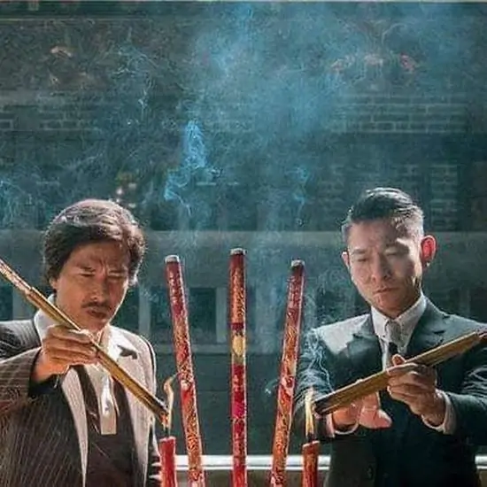 59 Hai người đàn ông cầm những nén hương lớn đứng giữa khói sương, hành động thành kính nhưng gương mặt lại mang đậm nét nghĩa khí của giới giang hồ.