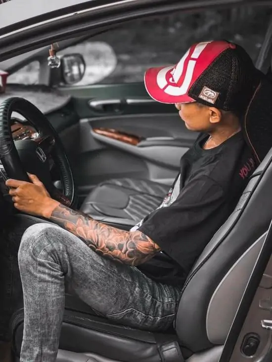 53 Nam thanh niên ngồi trong khoang lái xe hơi đời mới, đôi bàn tay xăm trổ cầm vô lăng thể hiện sự quyền lực và đẳng cấp vượt trội.