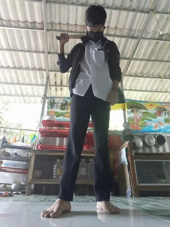 47 Người đàn ông cầm cây gậy gỗ đứng hiên ngang giữa sân, phong thái vững chãi như một người trong giới đang sẵn sàng cho một cuộc chiến.