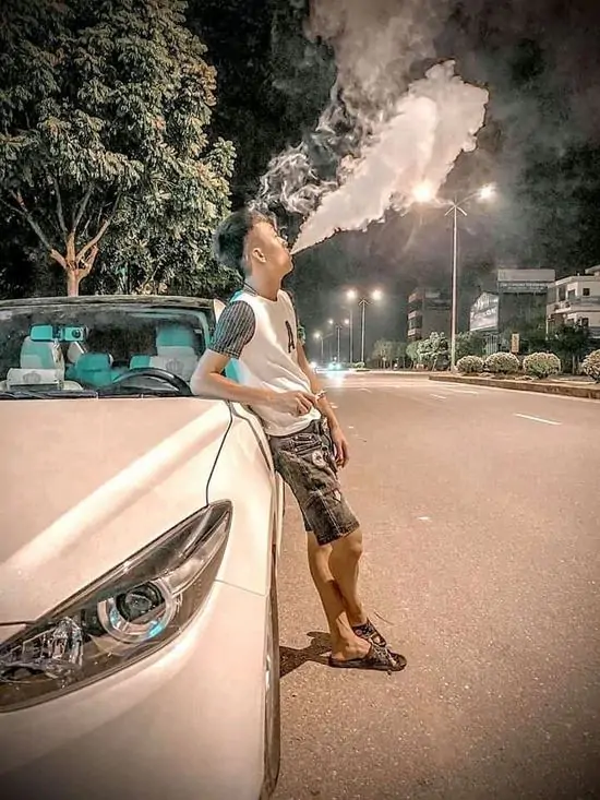 18 Gã thanh niên đứng dựa vào mui xe hơi, miệng ngậm điếu thuốc nhả khói trắng xóa tạo nên một khung hình cực kỳ cá tính và nổi loạn.