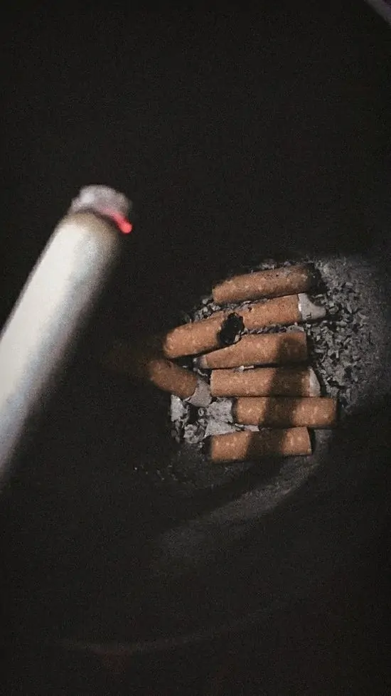 13 Ảnh profile điếu thuốc lá đang cháy giữa ngón tay với tro dài, khói bay thẳng, trong không gian tối om co ro.