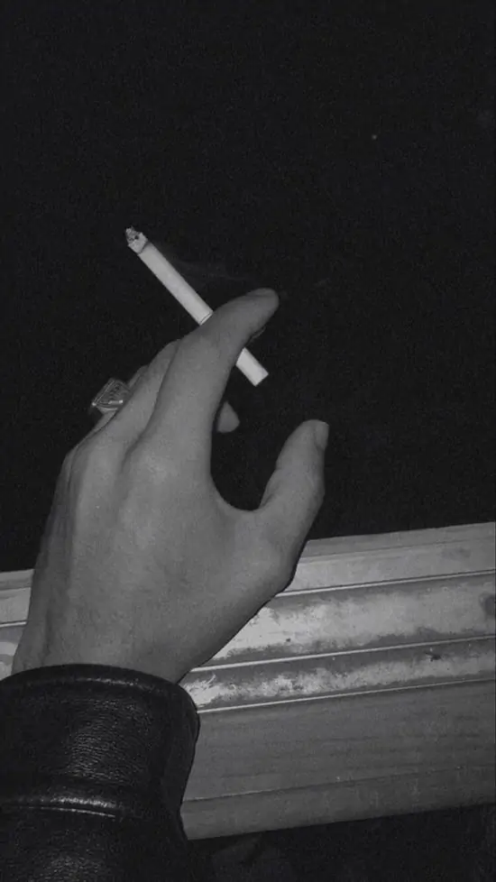24 Bàn tay cầm điếu thuốc trong bóng tối, khói bay lên từ đầu lọc, ngón tay đeo nhẫn, nặng nề trong khoảnh khắc thuốc lá trầm tư.