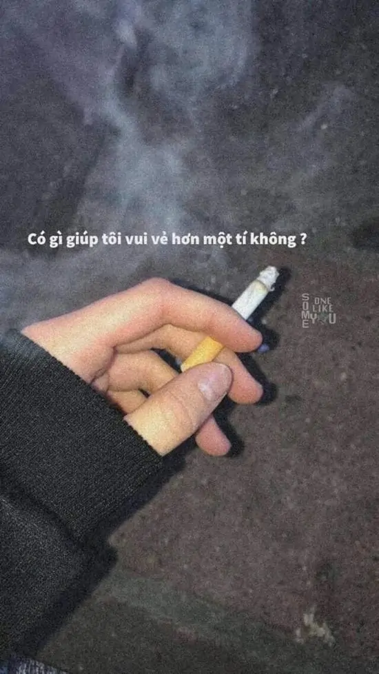2 Bàn tay nắm lỏng điếu thuốc lá giữa nền tối, khói bay lên kèm dòng chữ nhỏ phía trên, toát lên nỗi cô đơn.