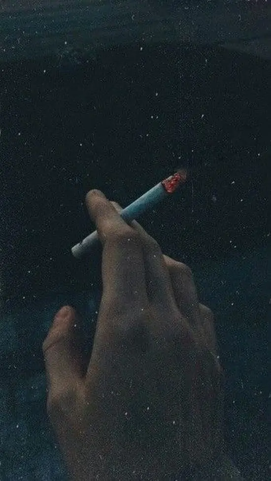 4 Góc chụp sát bàn tay với điếu thuốc cháy dở, khói cuộn nhẹ trong bóng tối dày đặc, gợi cảm giác day dứt.