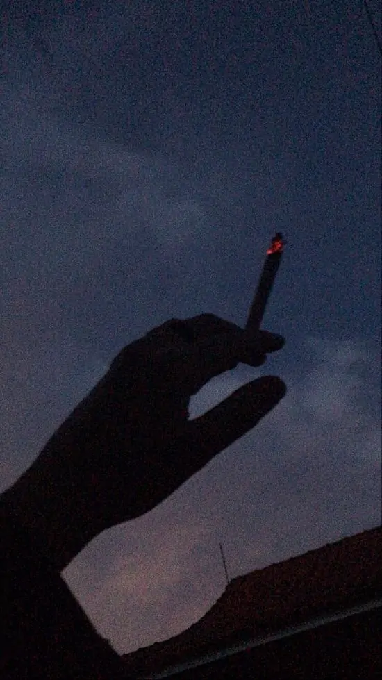6 Tay silhouette cầm điếu thuốc lá trước nền bầu trời hoàng hôn, khói bay thẳng lên cao mang vẻ xa xăm trong bức ảnh khói thuốc cô đơn.