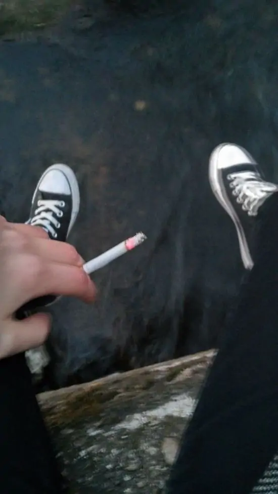 34 Chàng trai ngồi bệt trên sàn phòng với điện thoại trong tay, điếu thuốc kẹp môi, khói lan quanh vẻ chìm ngập.