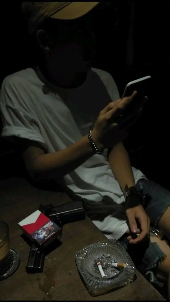 36 Bàn tay cầm lon nước và điếu thuốc đang cháy, khói bay nhẹ trong góc phòng, nặng nề.