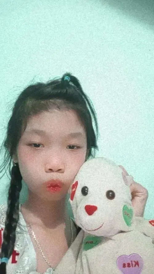 9 Bạn nữ ôm thú bông trắng, buộc tóc cao và chu môi trước nền tường xanh nhạt
