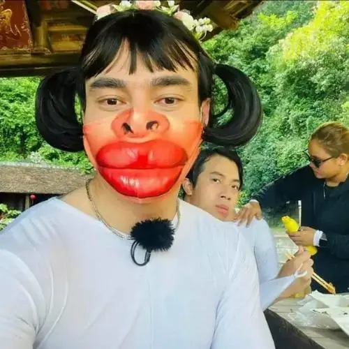 10 Giữa khung cảnh công viên, nhân vật hóa trang môi đỏ đứng sát máy với tóc buộc hai bên