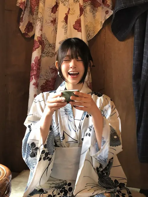 23 Bạn nữ mặc yukata ngồi trong quán ăn Nhật, cười tươi khi cầm điện thoại và đũa