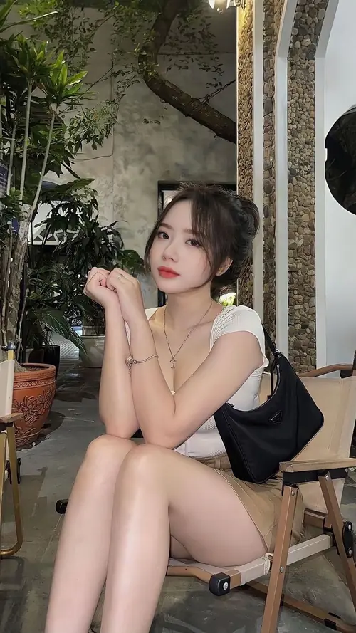 1 Gái xinh ngồi co chân ngoài hiên, tay chống cằm và nhìn sang bên phải.