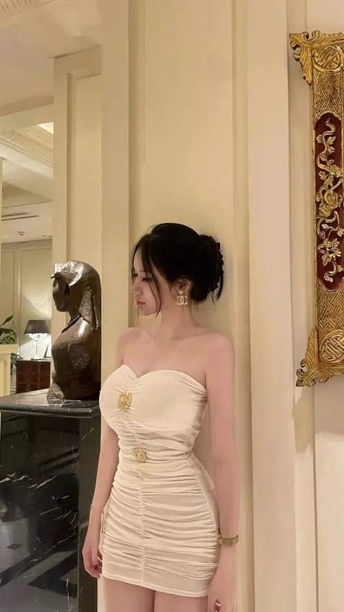 5 Chiếc váy quây màu kem ôm dáng, nhân vật nữ đứng nghiêng trong căn phòng có gương lớn.