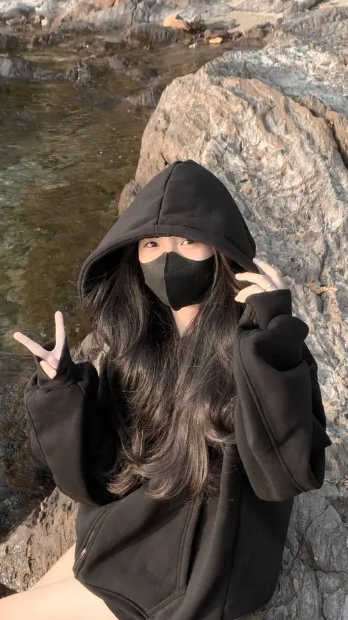 3 Cô bạn áo hoodie đen che mặt bằng khẩu trang, giơ tay tạo dáng bên mỏm đá nắng nhẹ