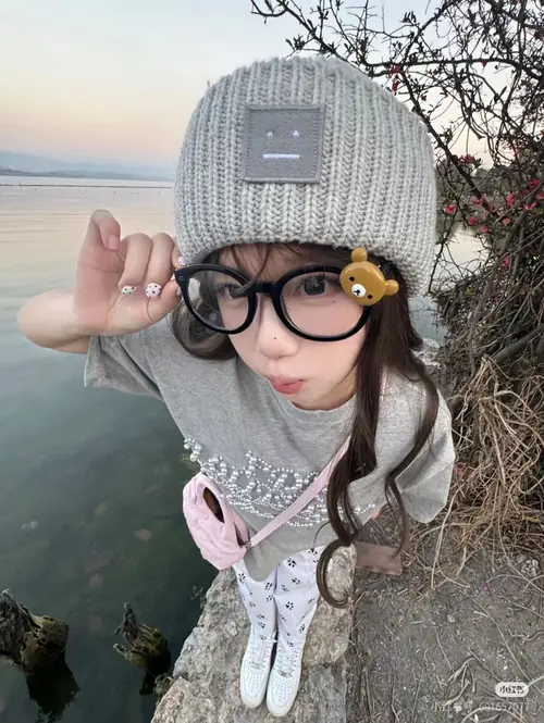 6 Bên bờ biển nhiều đá, cô gái đội beanie xám đeo kính tròn và vẫy tay nhỏ