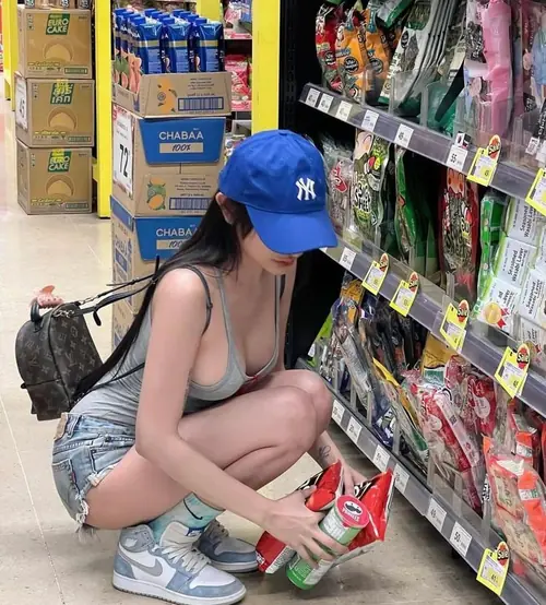 1 Cô gái đội mũ xanh ngồi chọn đồ trong siêu thị, áo ôm sáng màu và váy jean ngắn năng động