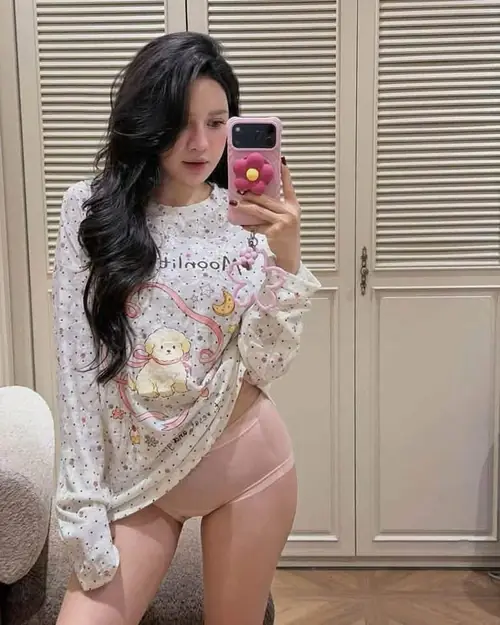 6 Trước tủ gỗ sáng màu, người đẹp tóc đen chụp gương với váy hoa ôm dáng và điện thoại hồng