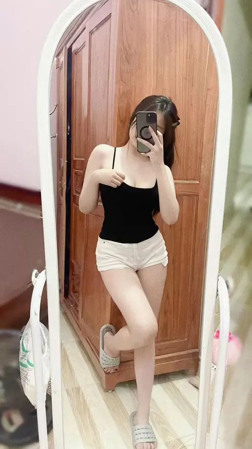 7 Cô gái đứng trước gương lớn, áo hai dây đen phối chân váy ngắn và tóc dài buông vai