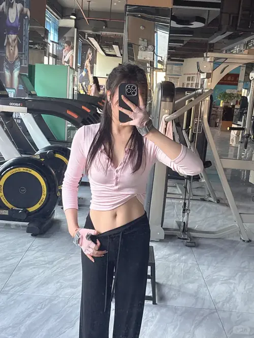 7 Cô gái trong phòng gym mặc áo lửng hồng quần đen che mặt bằng điện thoại trước gương