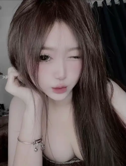 22 Mái tóc nâu dài rối nhẹ, bạn nữ đặt tay bên má khi ngồi trong phòng tối.