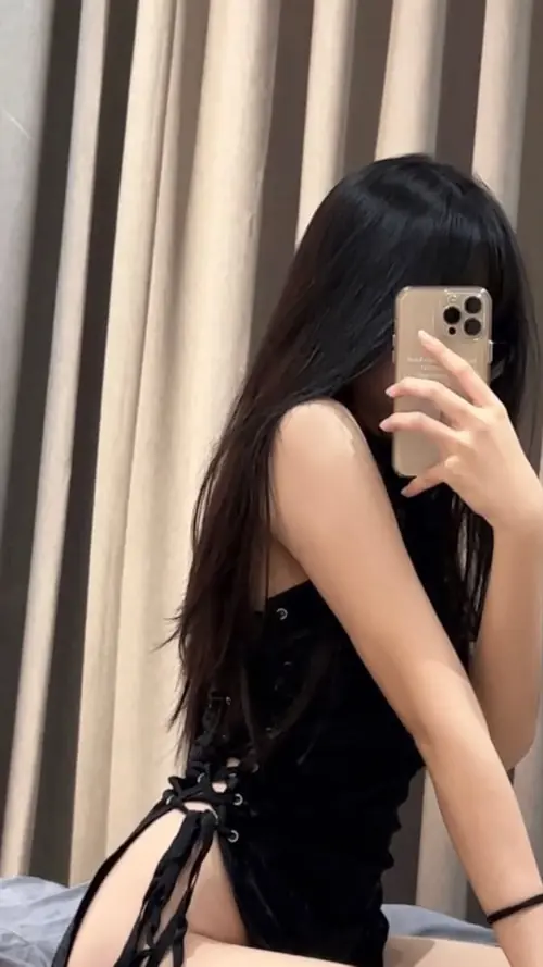 23 Ảnh gái xinh chụp gương với váy đen buộc dây bên hông và rèm sáng phía sau.