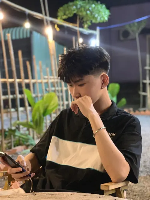 22 Bên bàn ăn ngoài trời, chàng trai áo sọc đen be chống tay gần miệng, tóc xoăn nhẹ