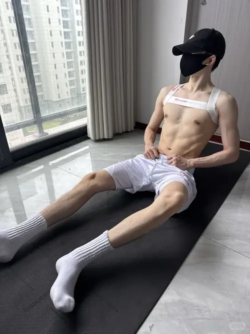 11 Chàng trai ngồi trên ghế cạnh cửa kính, đội mũ đen, khẩu trang và trang phục trắng thoải mái