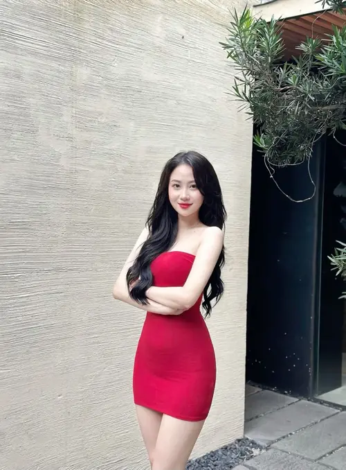 15 Cô gái váy đỏ đứng khoanh tay trước mảng tường xám, gương mặt hiền dịu và tóc thẳng
