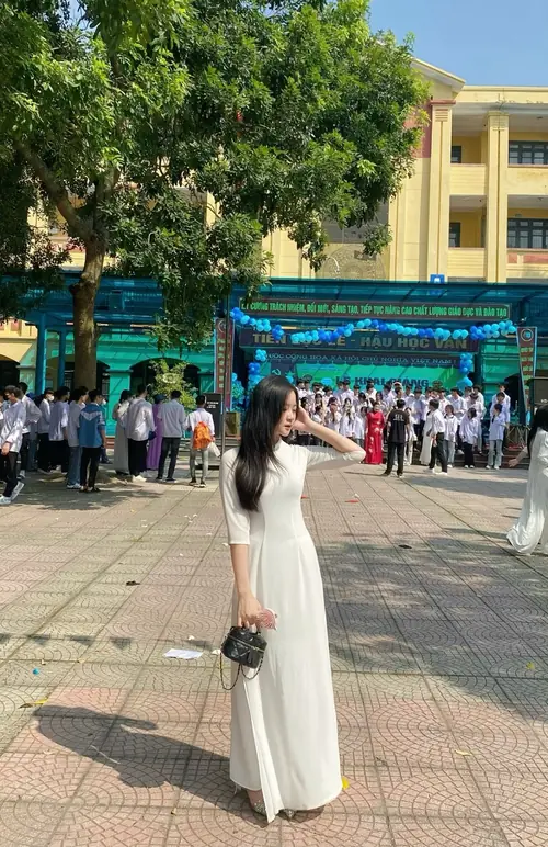 1 Trong sân trường rộng, ảnh nữ sinh cấp 3 ghi lại cô bạn áo dài trắng đứng trước hàng cây.