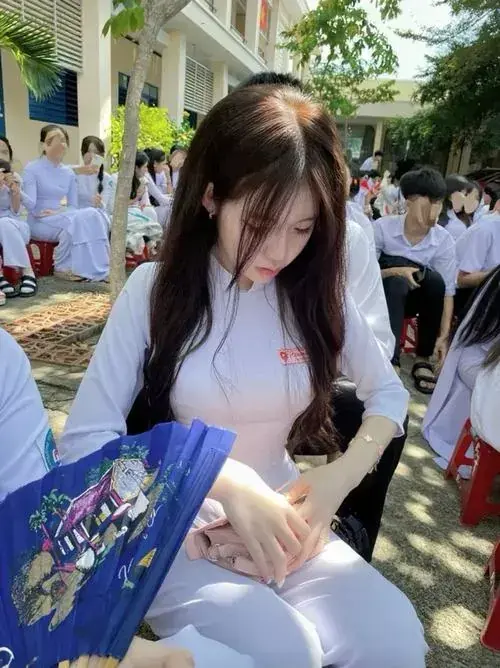 6 Giữa hàng ghế ngoài sân, nữ sinh trung học cúi nhẹ bên túi đồ xanh, tóc xõa che mặt.