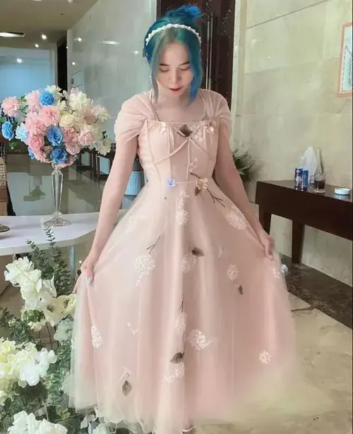 12 Trong váy công chúa hồng, nữ creator ngồi giữa hoa trang trí, tay chạm má và cười mềm