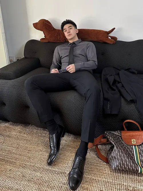 1 Chàng trai mặc đồ đen ngồi trên sofa xám, dáng thả lỏng với đôi boots da gọn gàng