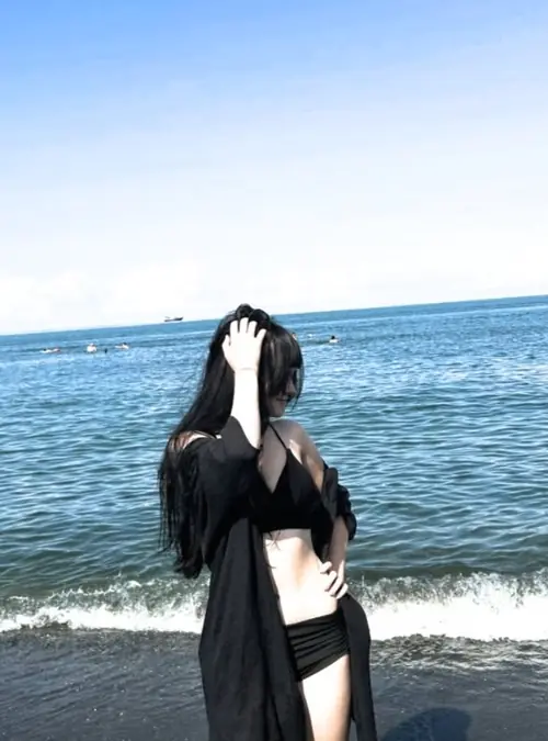 14 Bên bờ biển xanh, cô gái tóc dài mặc đồ đen đứng nghiêng trước sóng nước và trời sáng