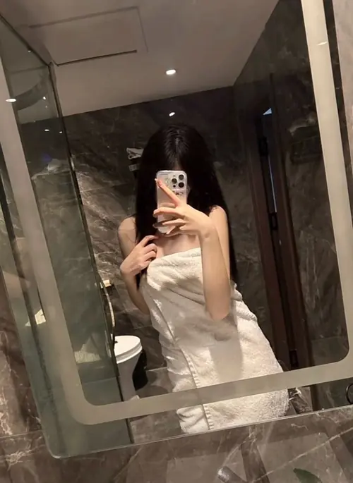17 Gương phòng tắm phản chiếu dáng đứng mặc đồ trắng, điện thoại che gần hết khuôn mặt.