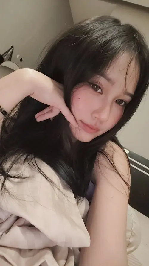 18 Cô nàng nằm trên giường, tay chạm tóc và áo khoác sáng màu phủ ngang vai.