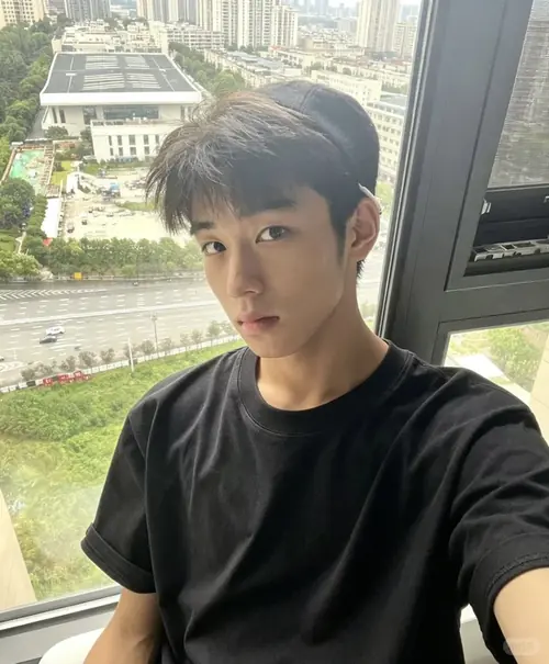 21 Chàng trai tóc ngắn chụp selfie cạnh cửa kính cao tầng, áo đen đơn giản và ánh nhìn thẳng