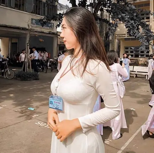 12 Giữa khu sân sinh hoạt, cô gái đeo thẻ tên mặc áo dài trắng, nhìn nghiêng dưới nắng chiều.