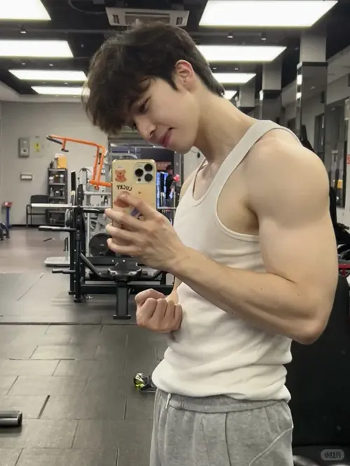 15 Ánh đèn phòng gym soi rõ body chuẩn, chàng trai mặc áo ba lỗ trắng và cầm điện thoại