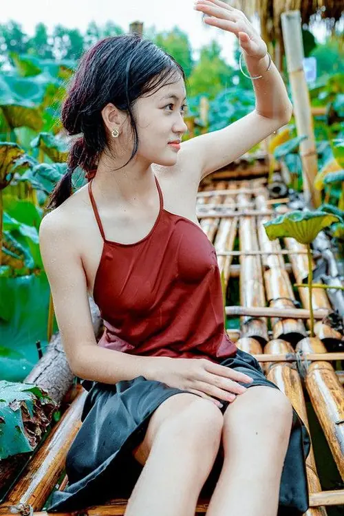 3 Cô gái áo hai dây đỏ ngồi giữa mảng xanh, mỉm cười nhẹ khi đưa tay chào