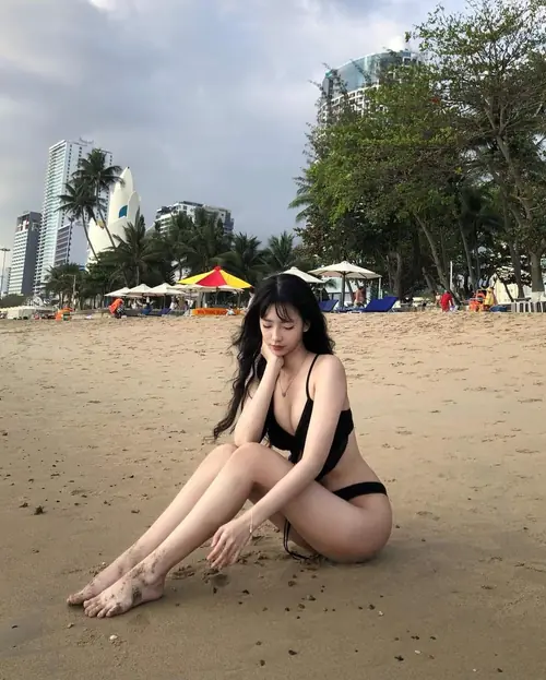 18 Người mặc bikini đen ngồi trên bãi cát, sau lưng có sóng biển và ô màu.