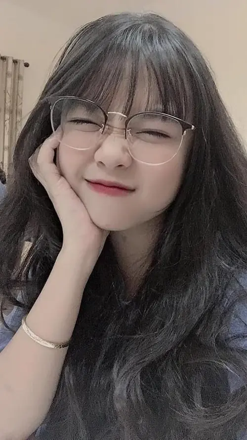 8 Cô bạn tóc dài chống cằm, mắt nhắm cười hiền sau cặp kính trong ở góc chụp gần