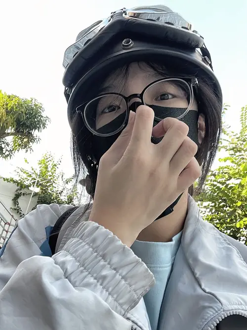 11 Mũ bảo hiểm đen phủ đầu, nàng kính cận che nửa mặt bằng tay áo giữa nền cây xanh