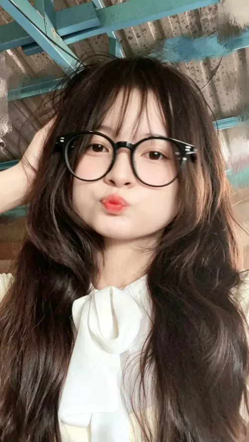 13 Cô nàng áo trắng ngồi trong quán, tóc xoăn dài và mắt kính đen đi cùng dáng môi chúm chím