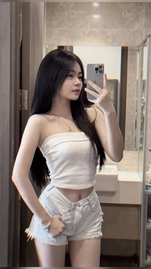 13 Điện thoại che một phần mặt, người mẫu đứng trước gương với áo quây trắng và quần short.