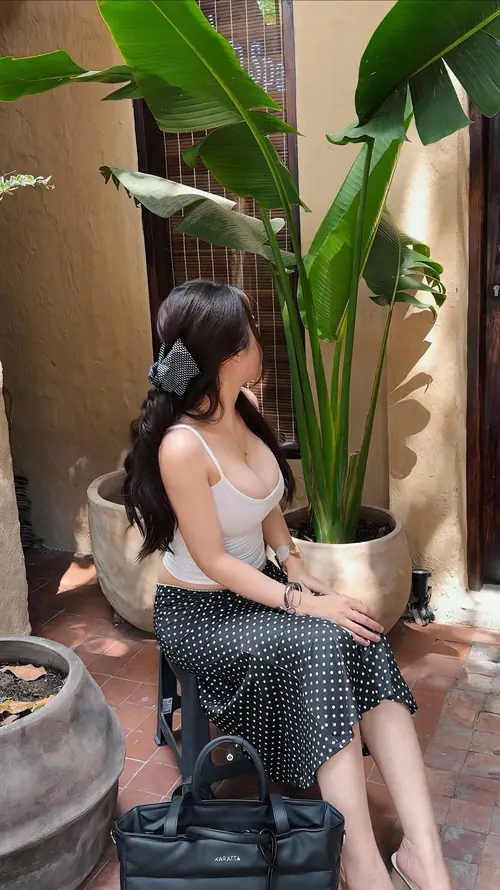 8 Giữa góc quán nhiều lá xanh, cô nàng ngồi nghiêng trên ghế, áo dây đen phối váy chấm bi