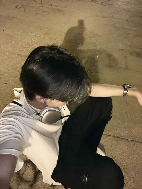 18 Trên nền đất vàng, chàng trai áo xám cúi sát gối, tai nghe trắng nằm quanh cổ